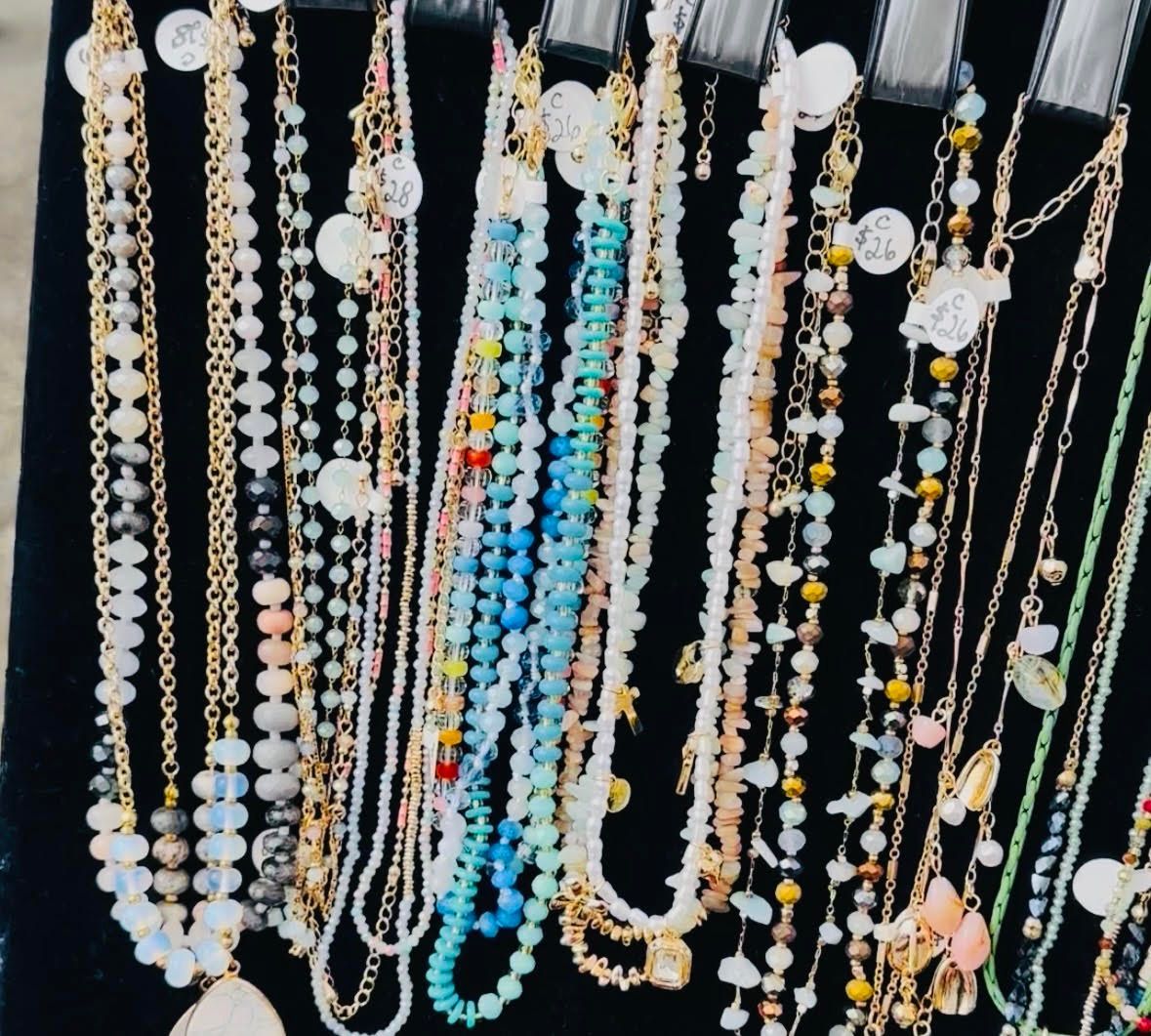 Rows of hanging beaded necklaces and charms in white, gold, blue, and pastel colors