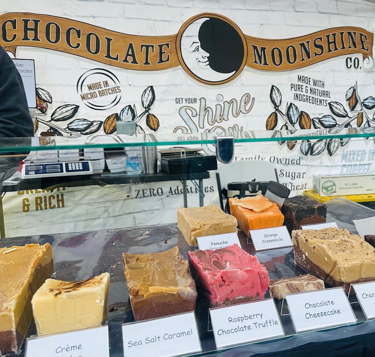 Chocolate moonshine candy display with assorted fudge and chocolate slices on a market stall.