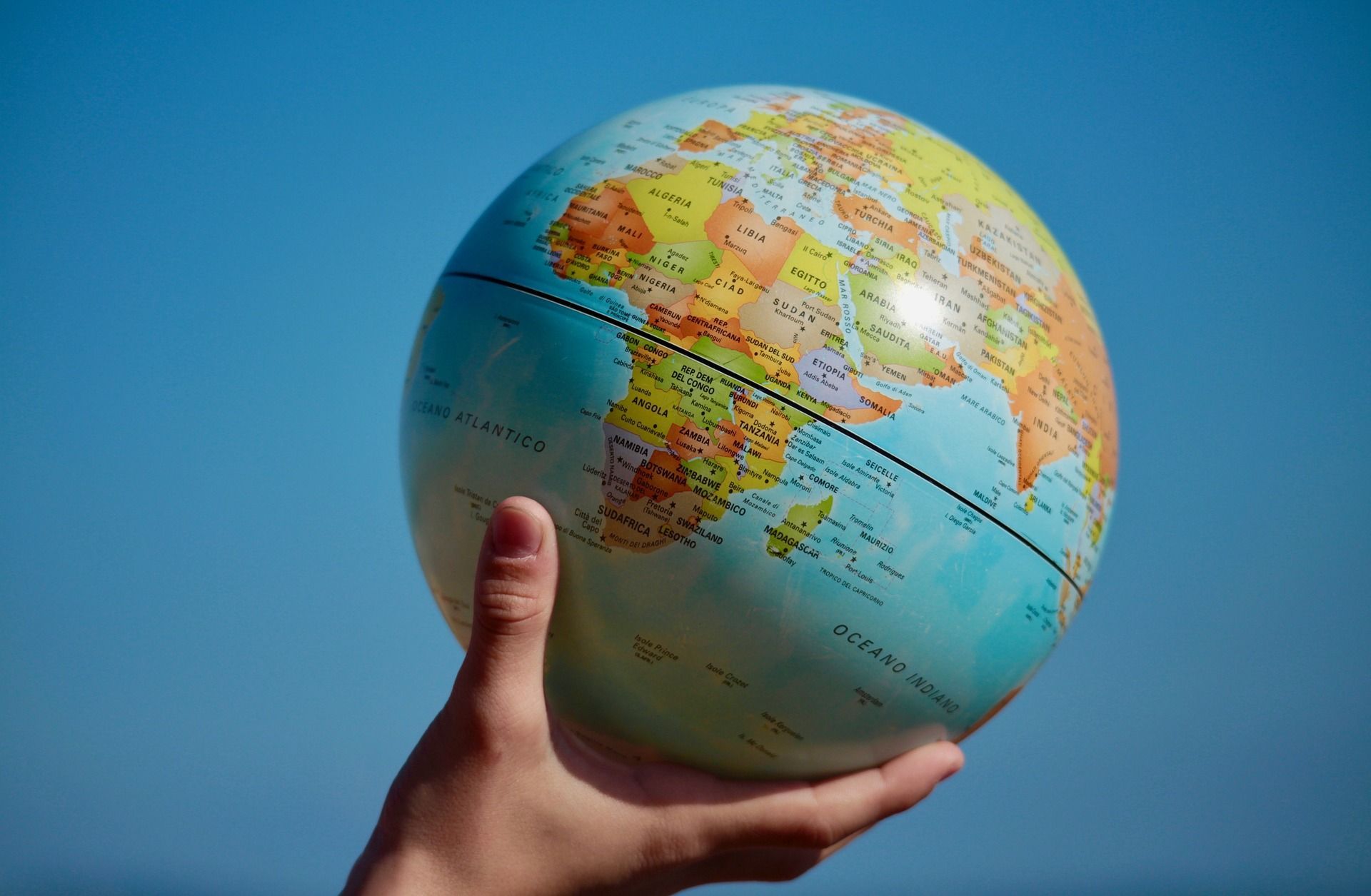 Hand holding a globe against a blue sky.