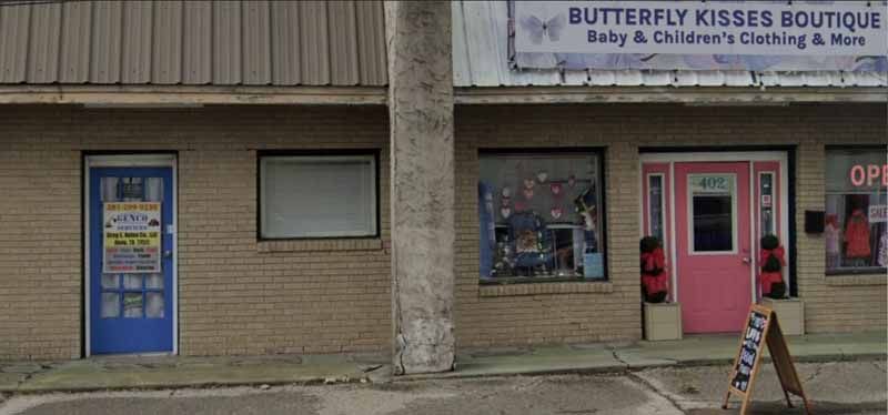Shops in a brick building: blue door, window, Butterfly Kisses Boutique with a pink door.