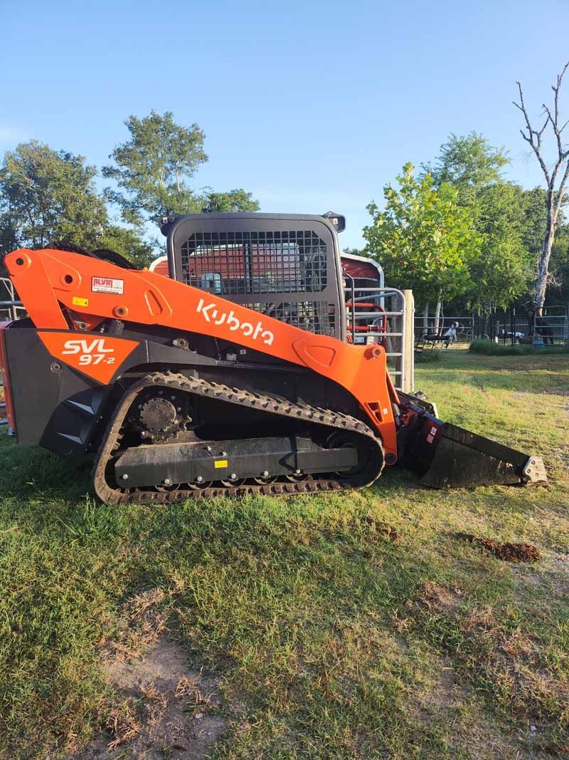 Orange Kubota SVL75-2 tracked skid steer on a grassy field with a brush cutter attachment.
