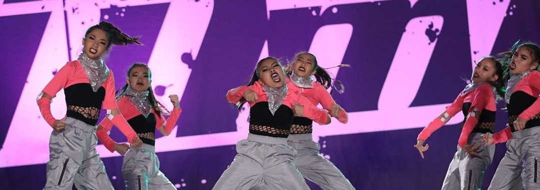 A group of young girls are dancing in front of a large purple sign.