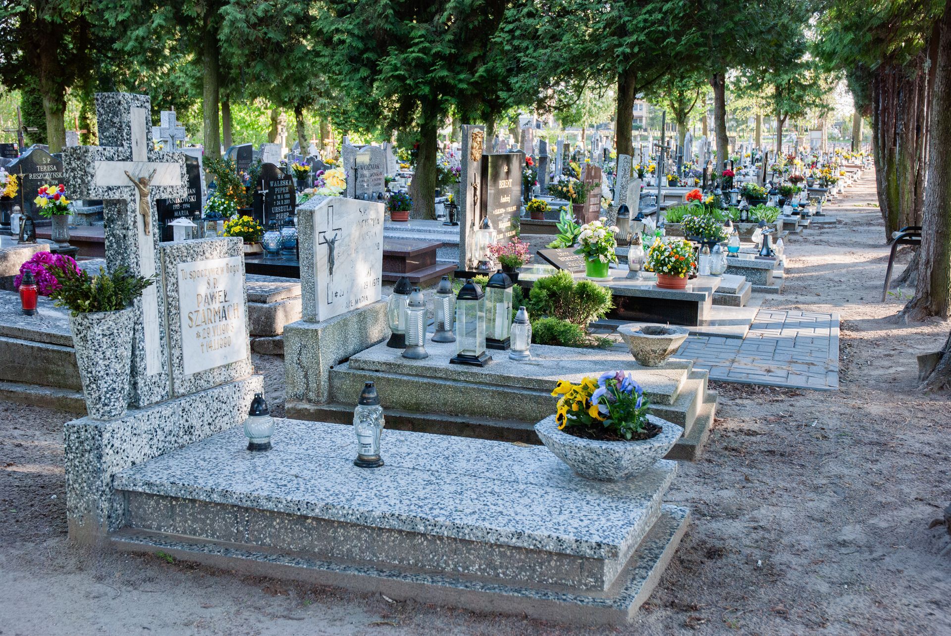 Peaceful cemetery with granite monuments and colorful flowers amidst tall trees.