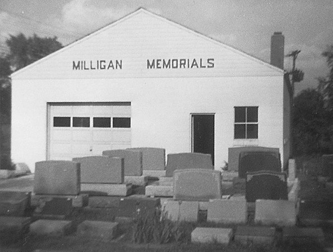 Milligan Memorials storefront with headstones in front. White building, garage door, sign above door.