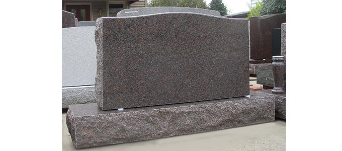A dark granite headstone, rectangular, on a matching base. Other headstones are in the background.