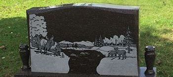 Dark headstone with etched scene of wildlife near a river.