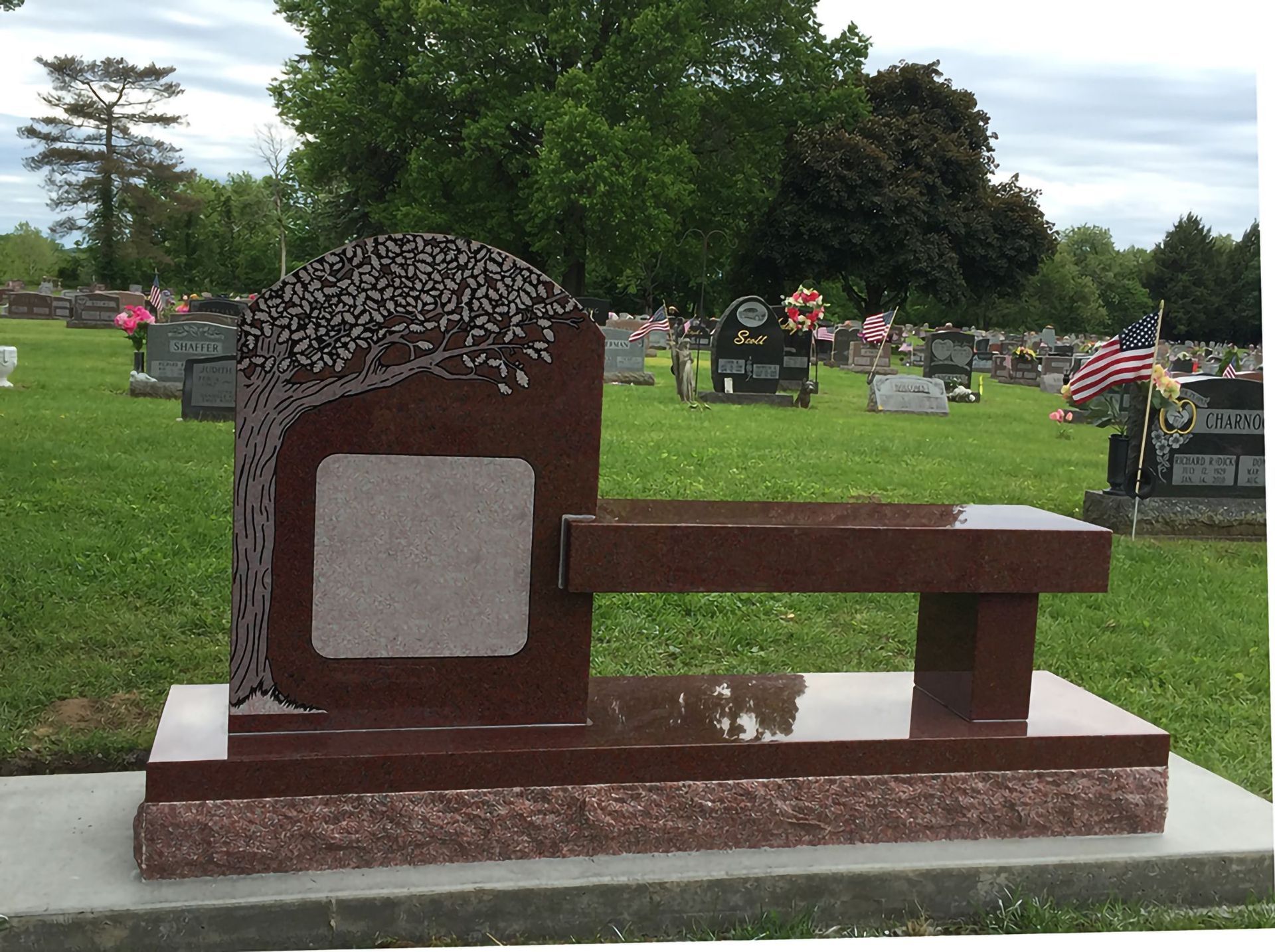 Red granite memorial with tree design, bench in cemetery.