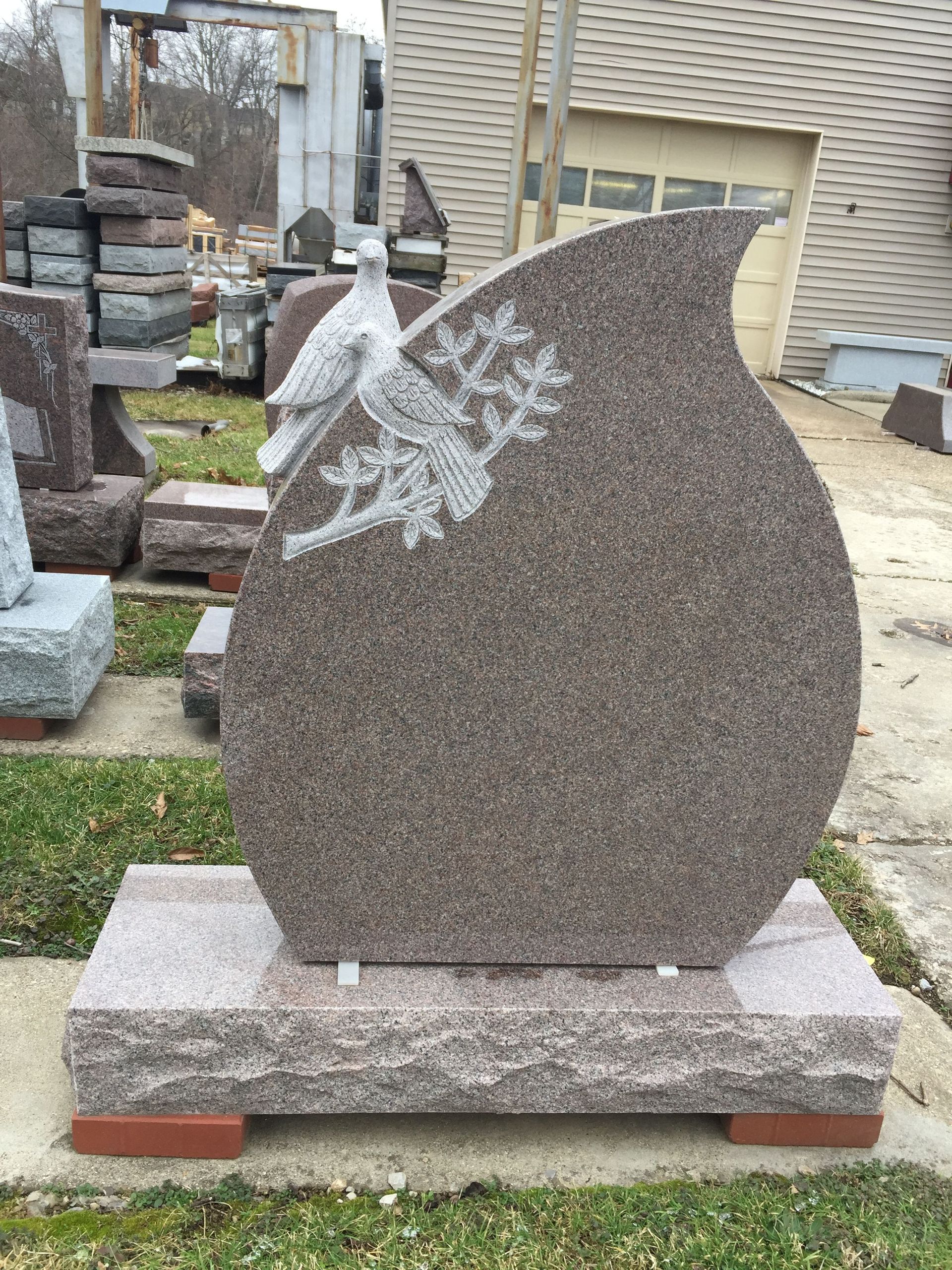 Brown granite memorial with dove and branch carving, set on a stone base.