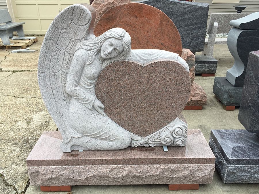 Angel statue embracing a heart-shaped monument; made of stone; outdoors.