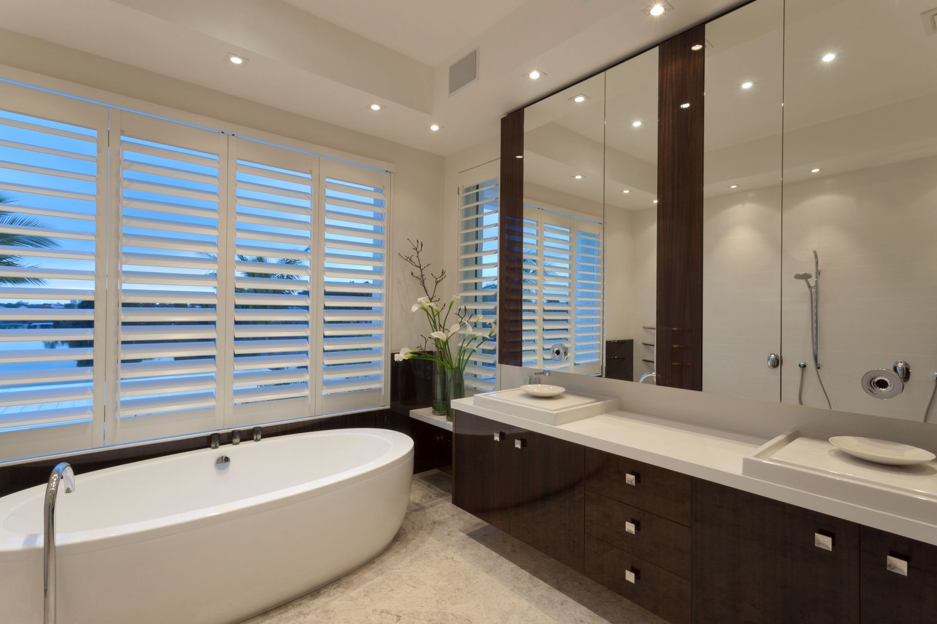 A bathroom with a tub, sink, mirror, and shutters