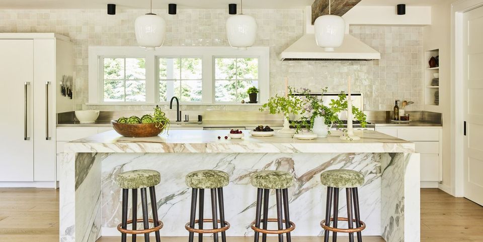 A kitchen with marble counter tops , stools , and a large island.