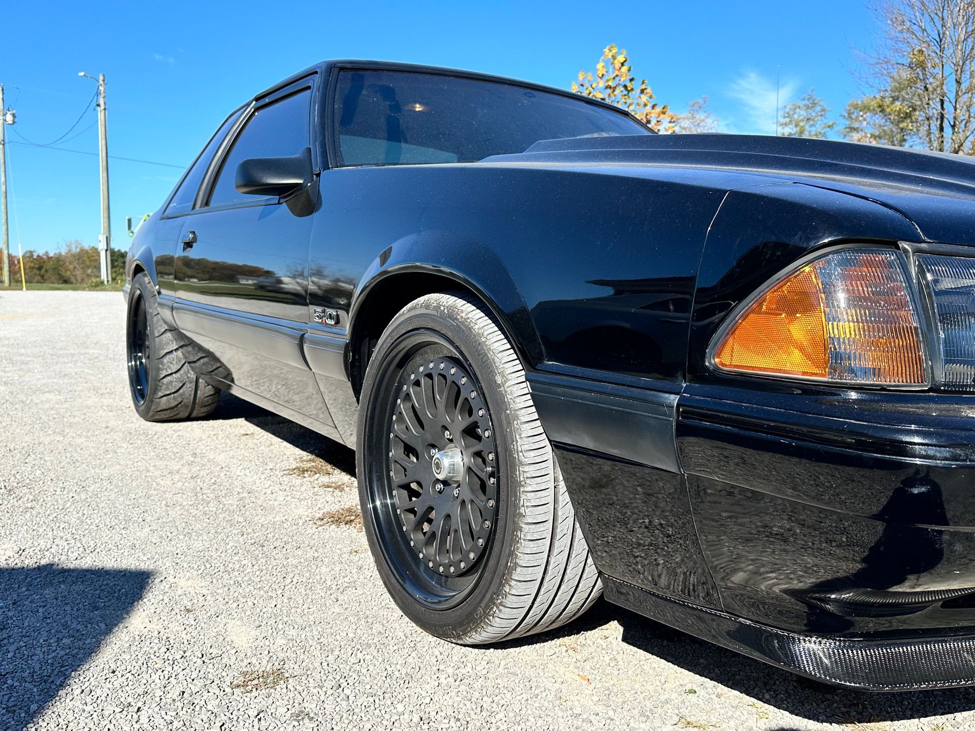 Black Ford Mustang with black rims on a gravel surface, under a bright, sunny sky. | Midwest Tire & Service LLC