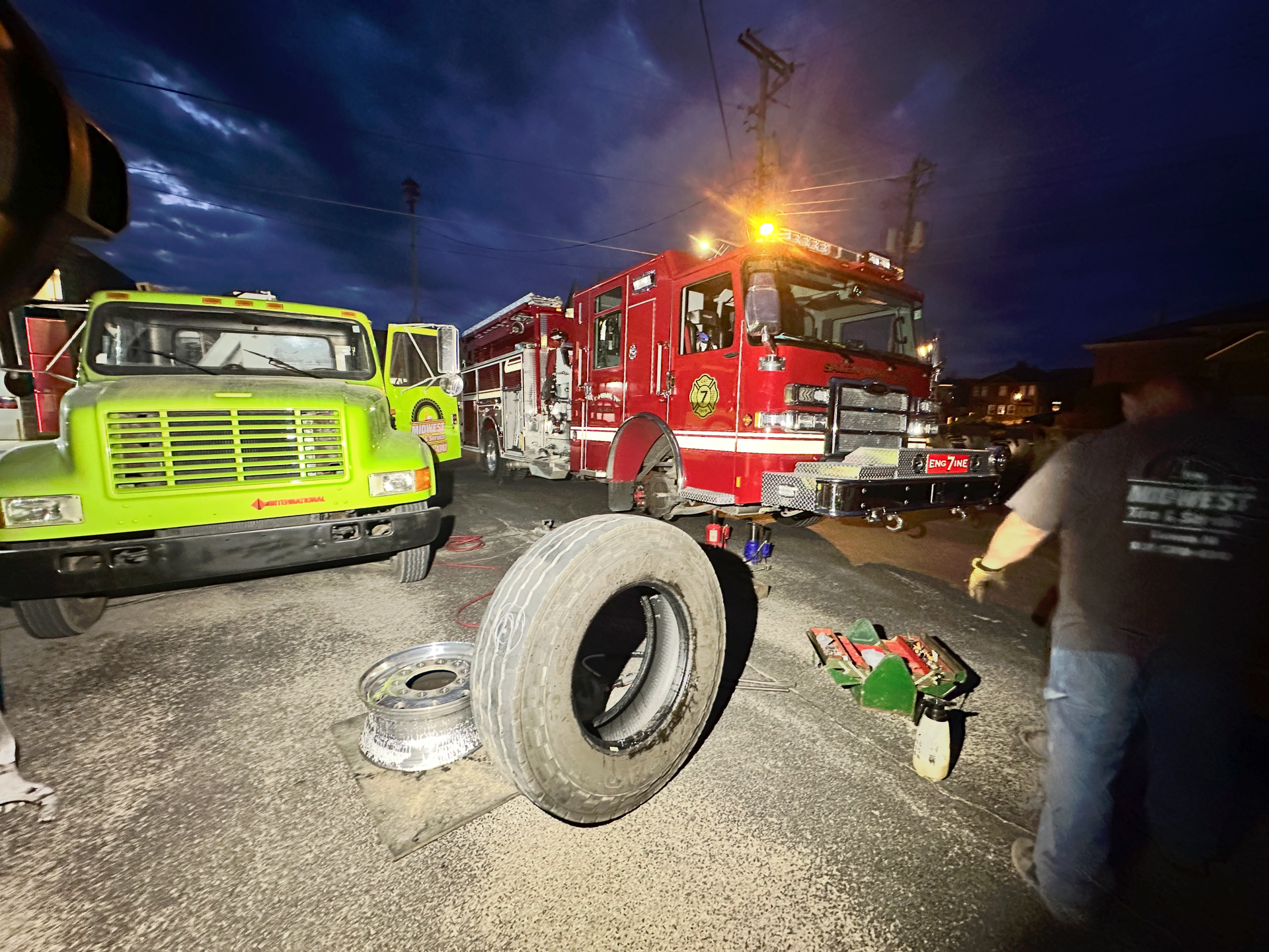Fire truck at night scene with green truck, tire, and person. | Midwest Tire & Service LLC