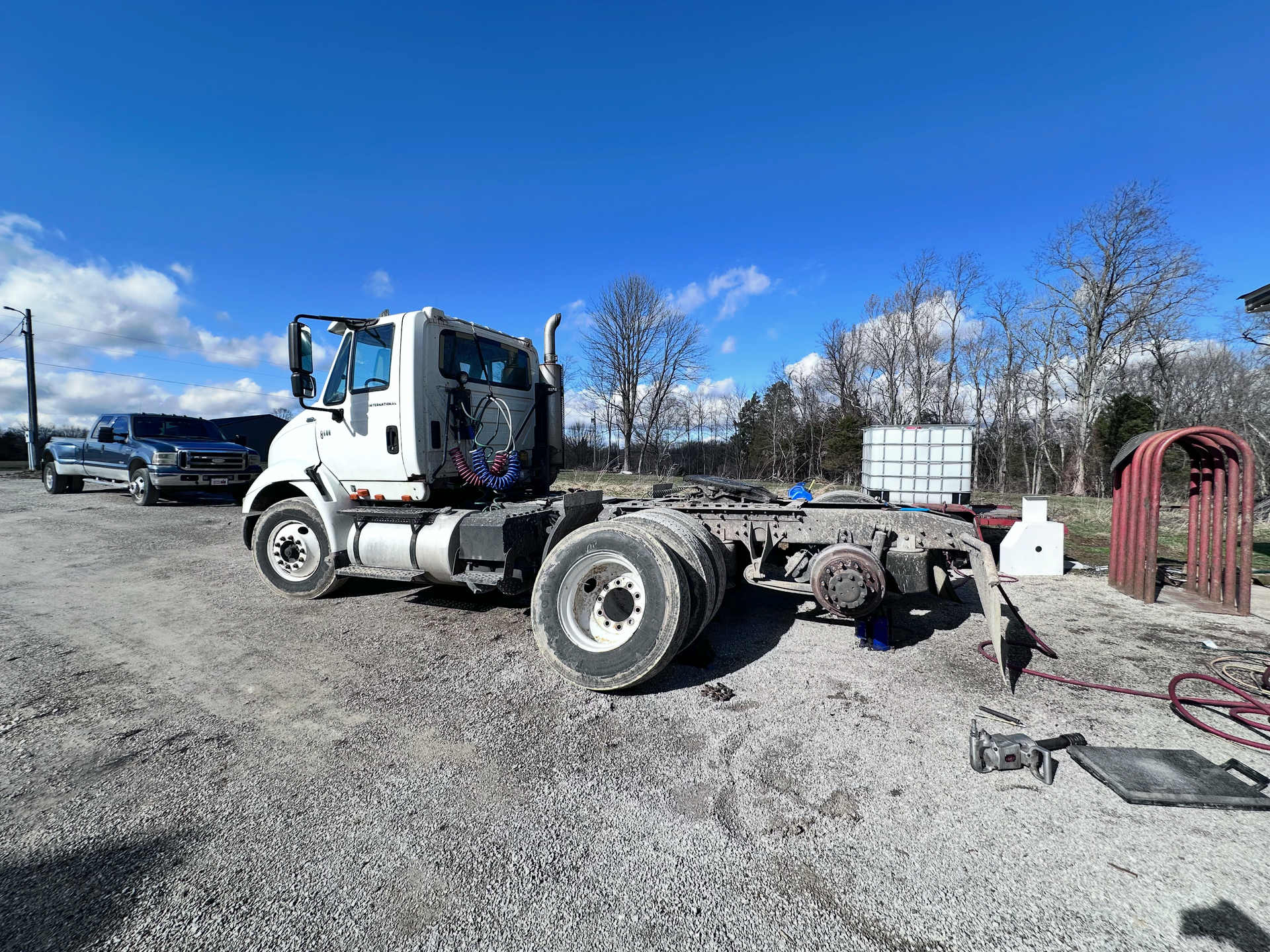 White cab-over truck chassis parked on gravel with blue sky and some trees in the background. | Midwest Tire & Service LLC