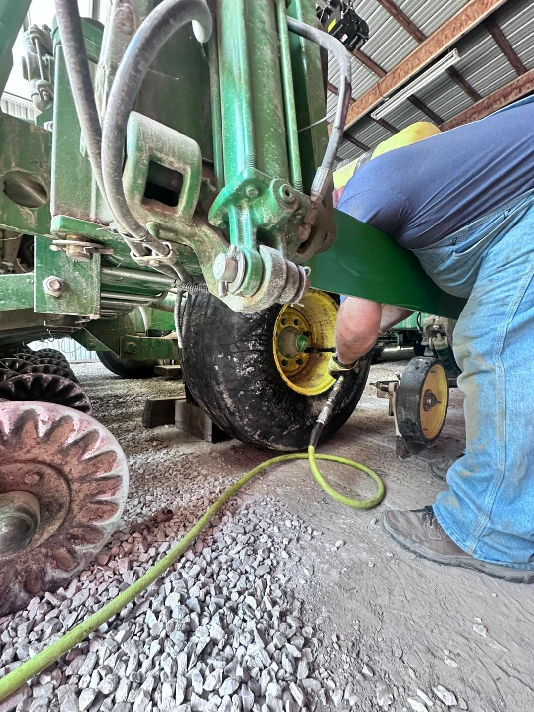 Man Inflating Tire on a Green Farm Machine Inside a Building | Midwest Tire & Service LLC