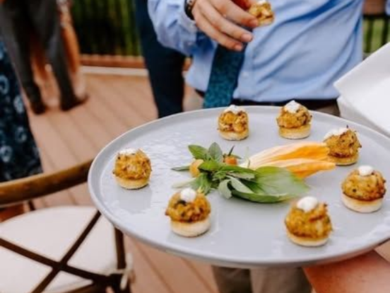 Plate of appetizers for catering event in Annapolis, MD. The plate has crab cakes topped with sauce, herbs & yellow flowers.