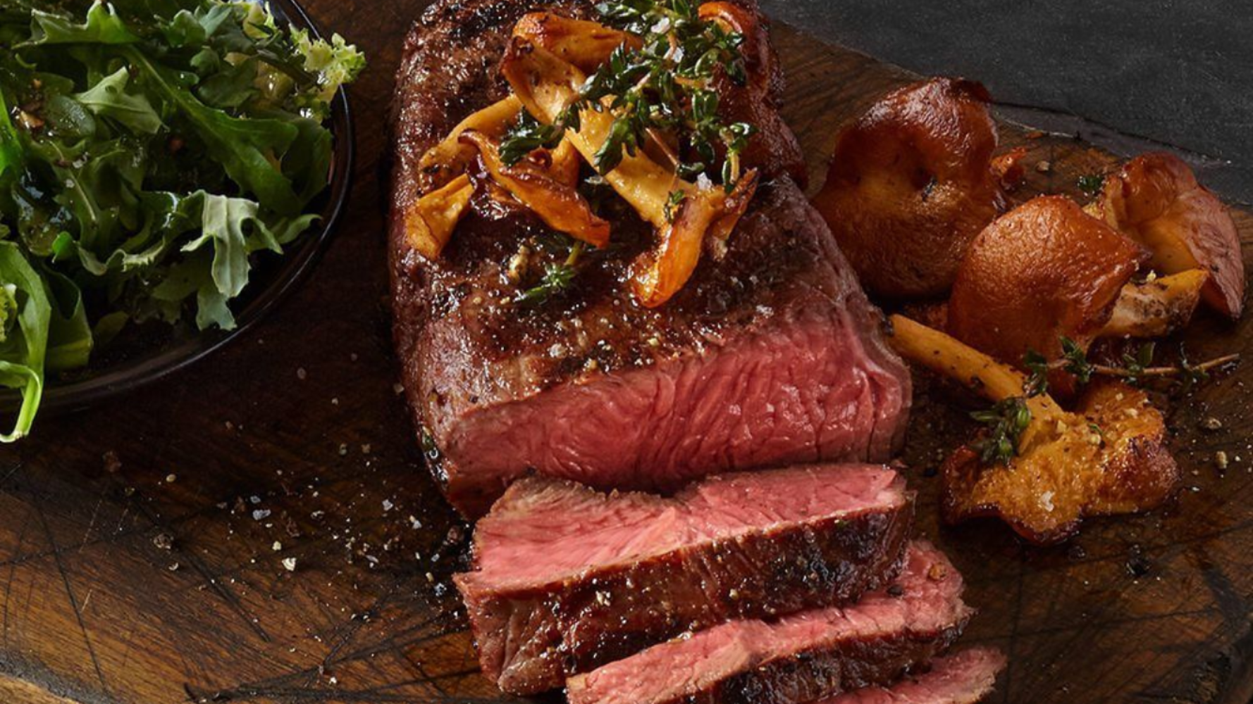 Sliced steak for a wedding carving station topped with mushrooms, served with greens and sauteed mushrooms.