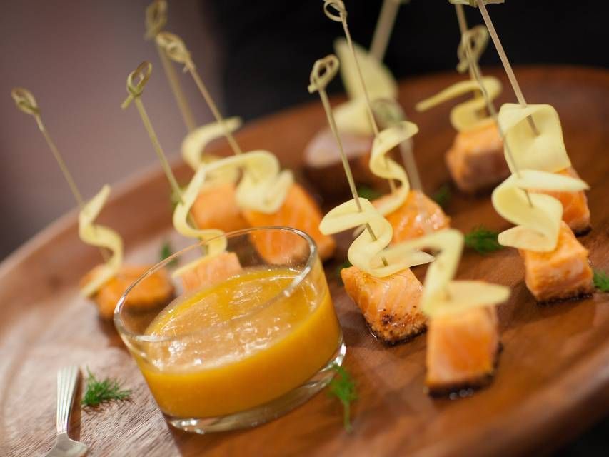 Salmon appetizers with cucumber ribbons, yellow sauce, on a wooden platter.
