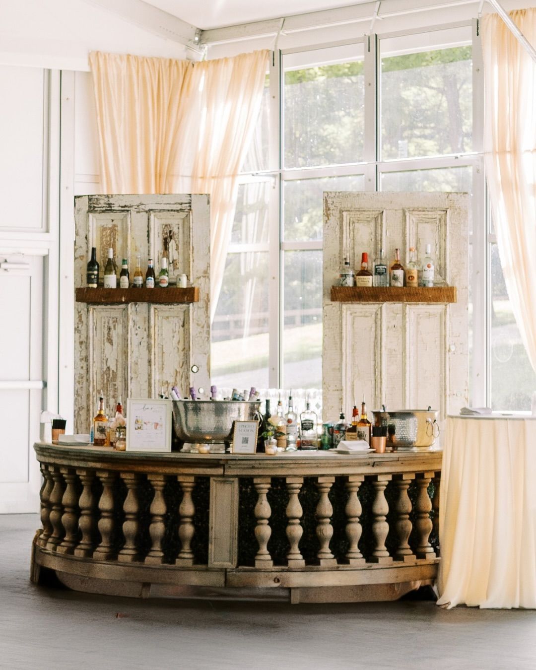 Rustic bar set in front of large windows with draped curtains, and vintage door shelves for an Annapolis Catering Event