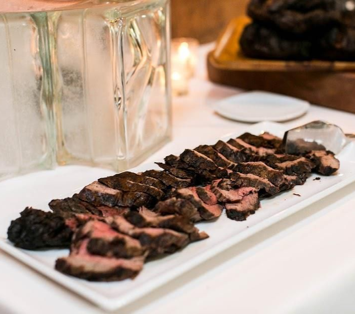 Sliced, expertly-prepared meat on a white rectangular platter, near a clear block and small plates.