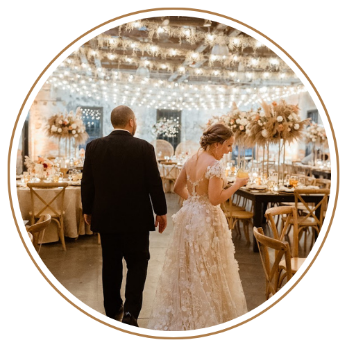 Bride and groom walking in a decorated reception hall with tables and floral arrangements.
