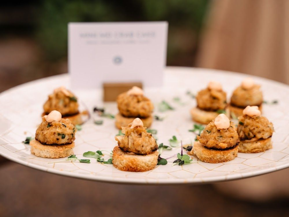 Crab cakes on toasted bread with sauce on a platter, held outdoors from a caterer in Maryland