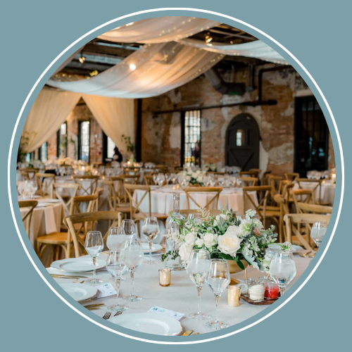 Wedding reception in a brick building with draped fabric, tables set with flowers and glassware.