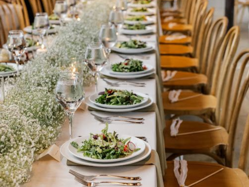 Long dining table set for a meal, floral centerpieces and salads on white plates for a plated wedding dinner in Annapolis, MD