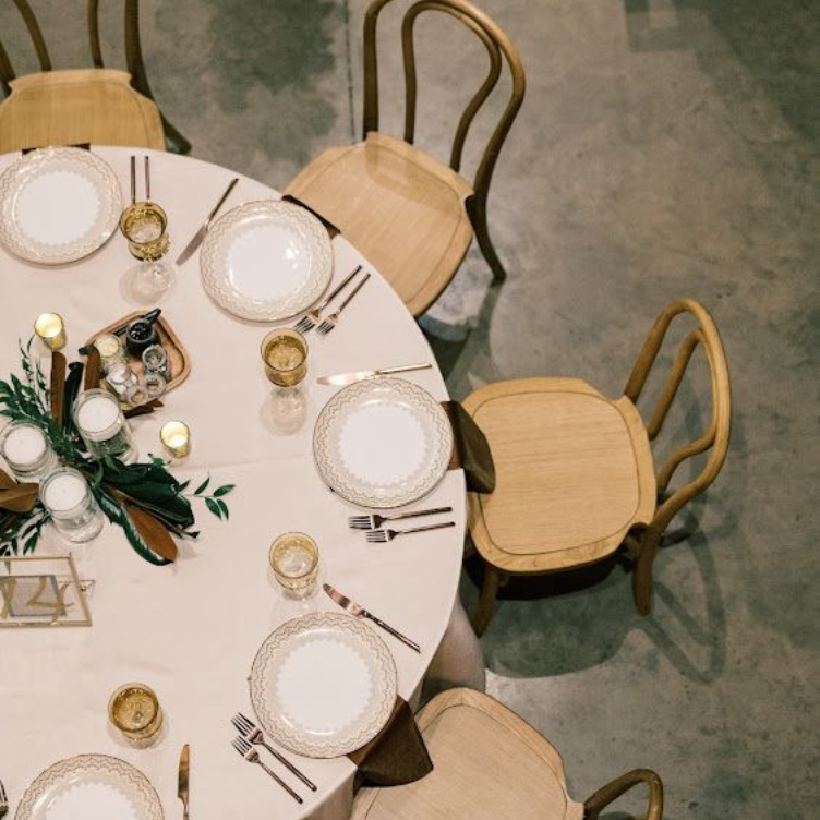 Round table set with plates, glasses, and silverware. Chairs surround it, ready for a meal.