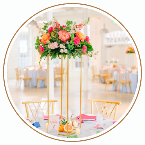 Gold floral centerpiece on a table, brightly colored flowers, formal dining setting, golden legs, pink accents.