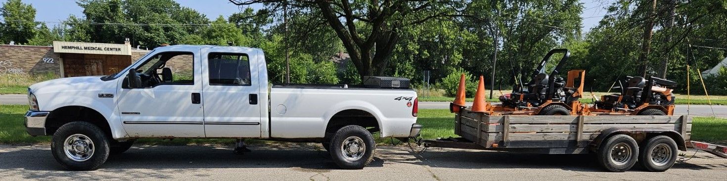 A white truck is towing a trailer with a tractor on it.