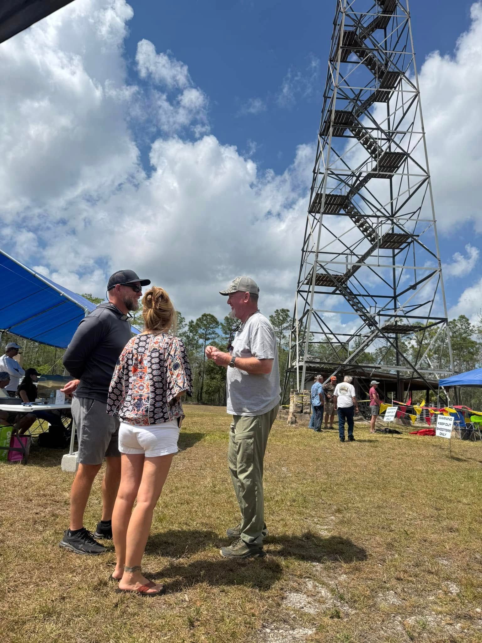 A group of people are standing in a field in front of a tower.