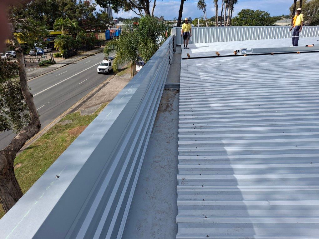 Metal roof edge with workers; road and trees in background.