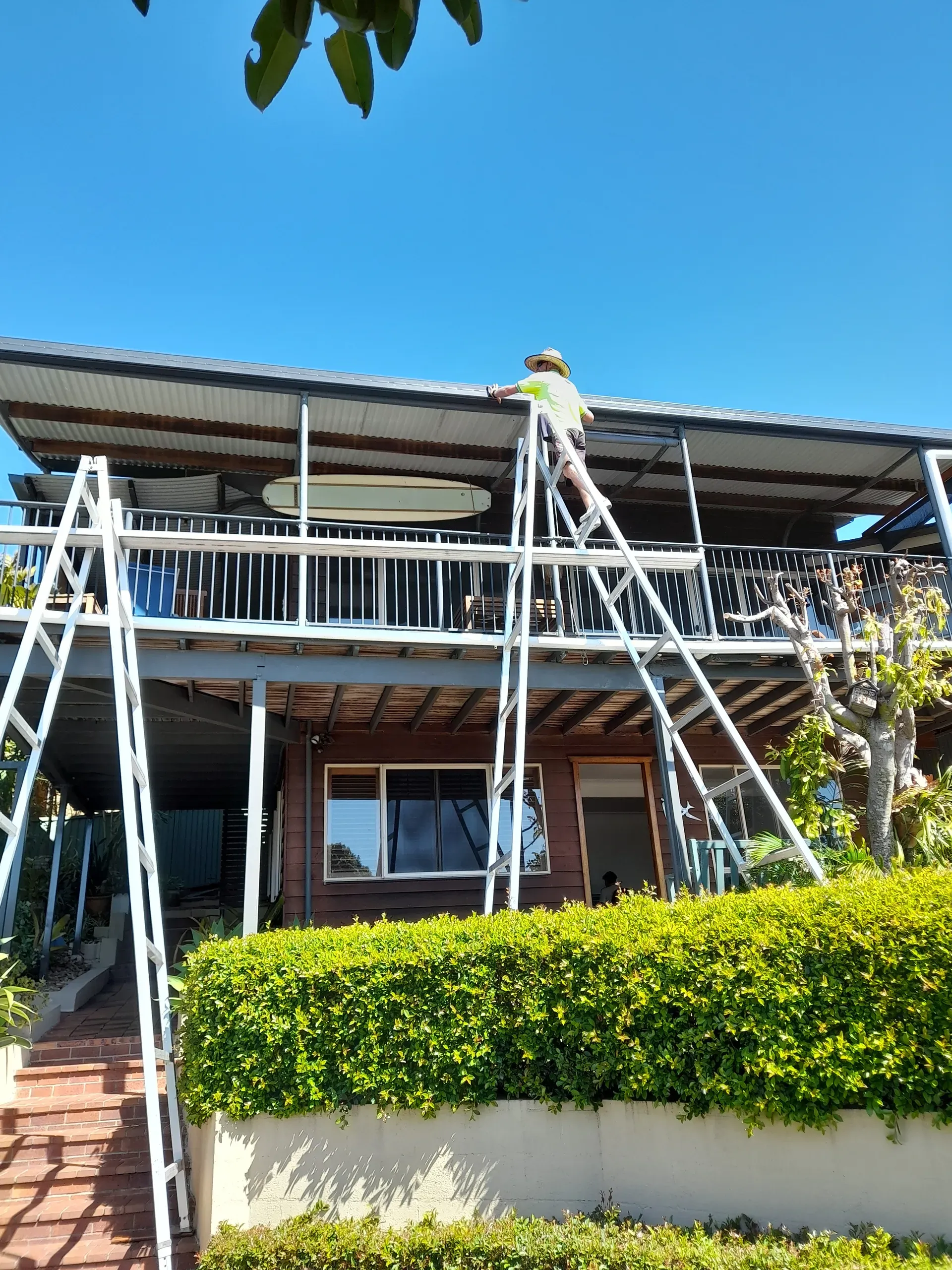 Person on a ladder repairing a home's roof on a sunny day.