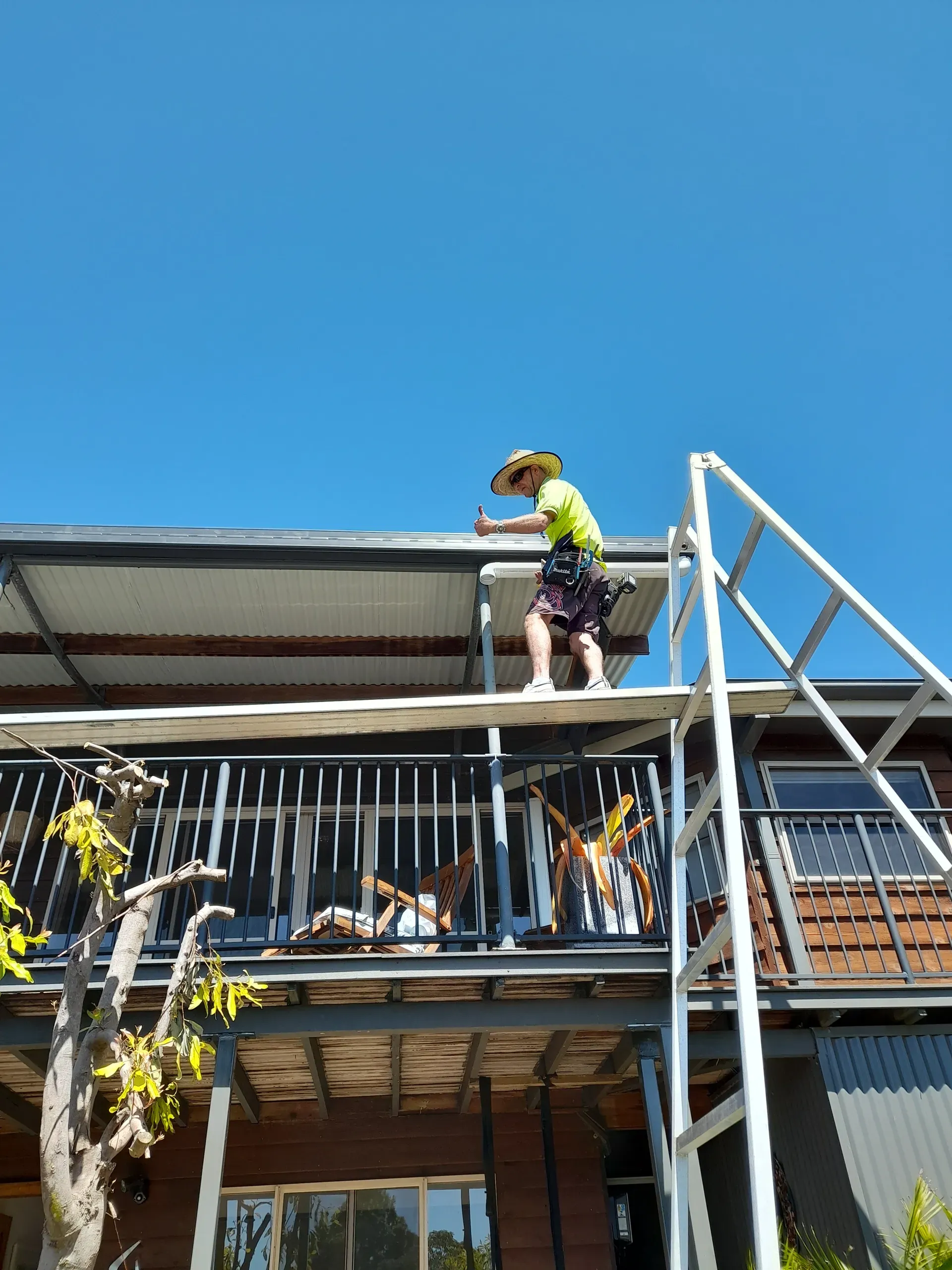 Person on a ladder, working on a roof. Bright blue sky.