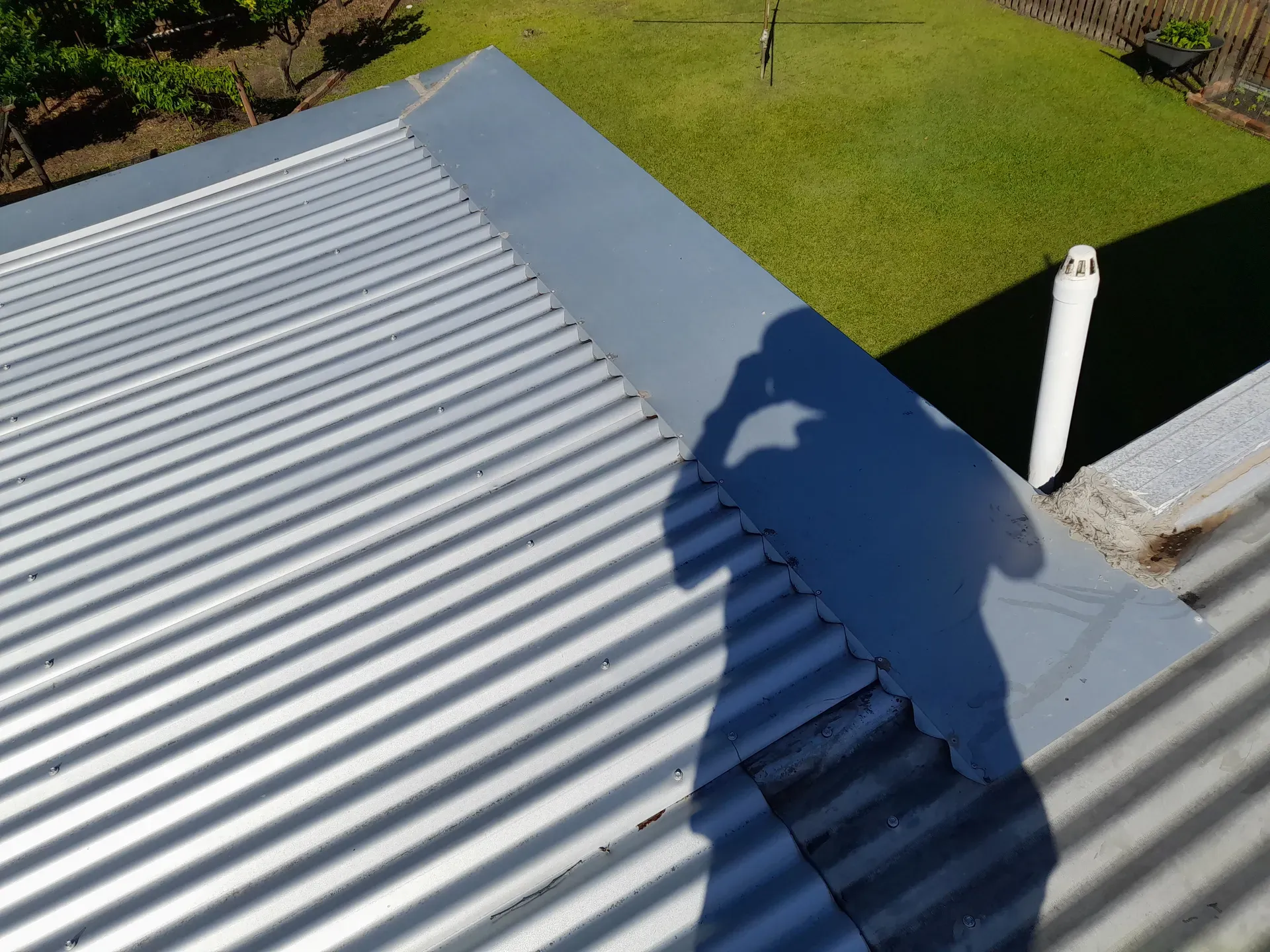Corrugated metal roof with grey trim, casting a shadow onto the grass. White pipe in the corner.