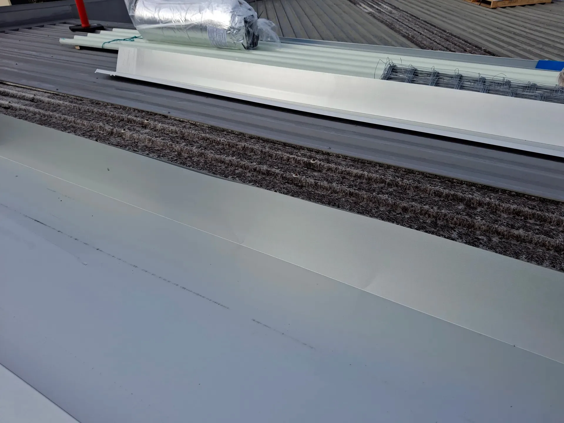 Metal roofing materials and insulation on a rooftop, viewed from a close-up perspective.