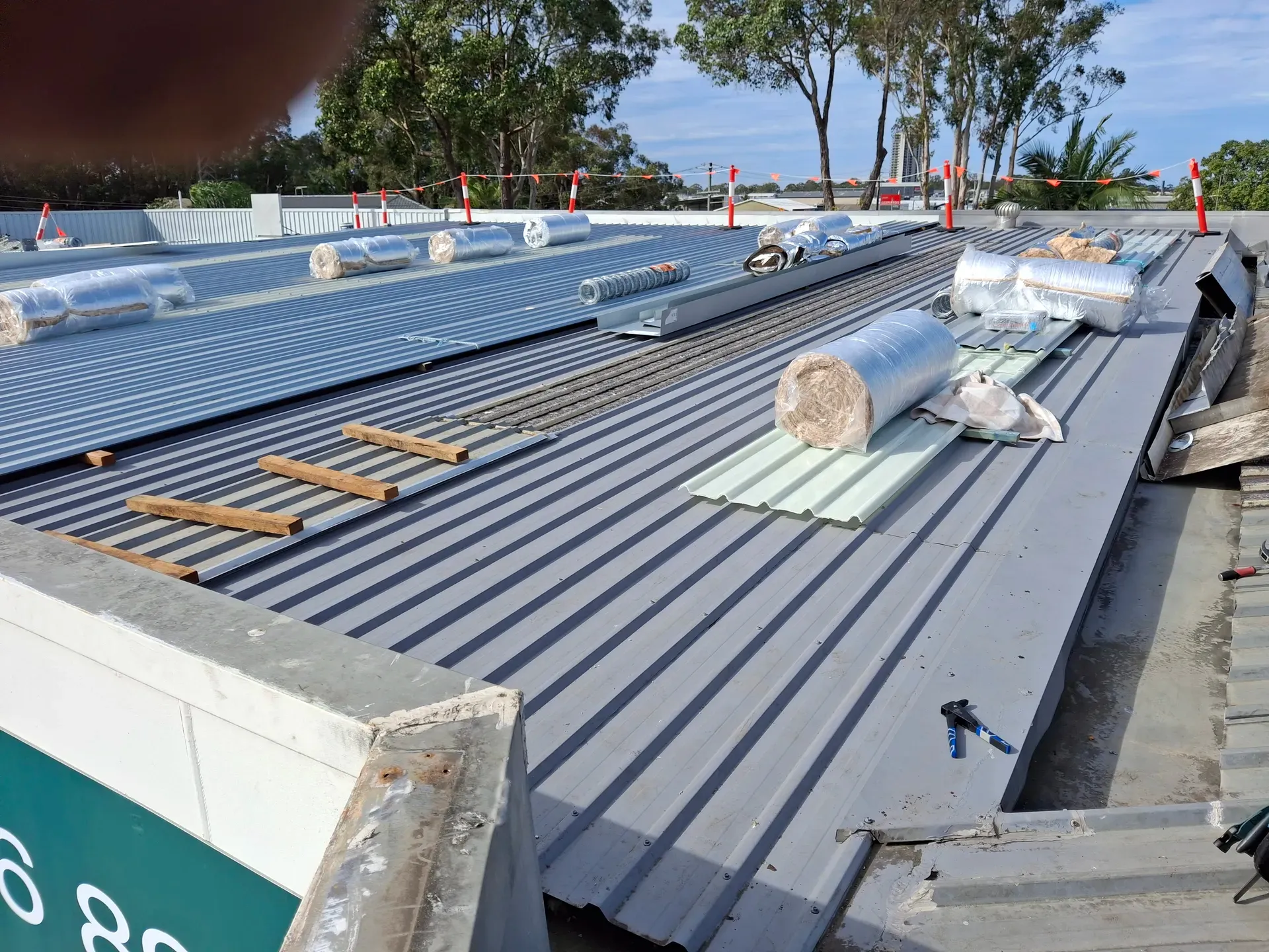 Metal roof under construction; rolls of insulation and panels on a flat roof.