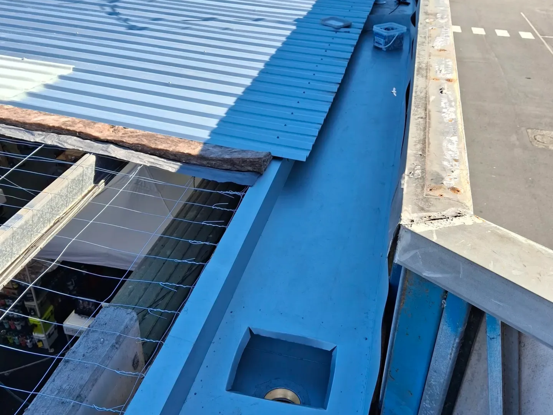 Blue-painted gutter along building edge, with metal roofing and street visible.