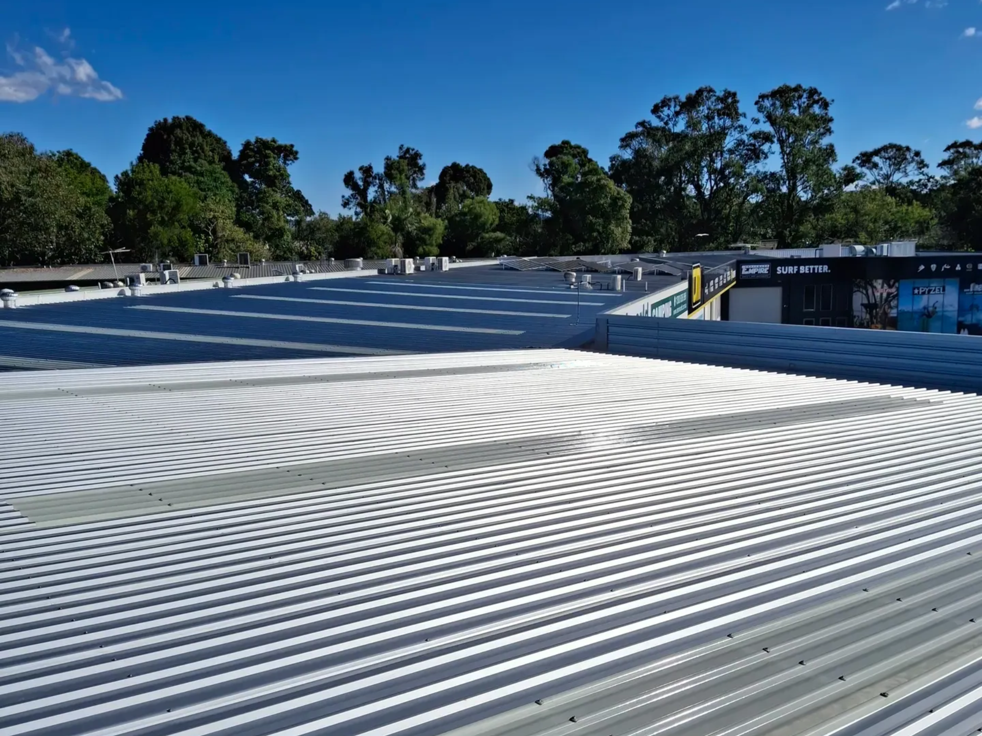 Corrugated metal roof on a building, blue sky, trees in the background.