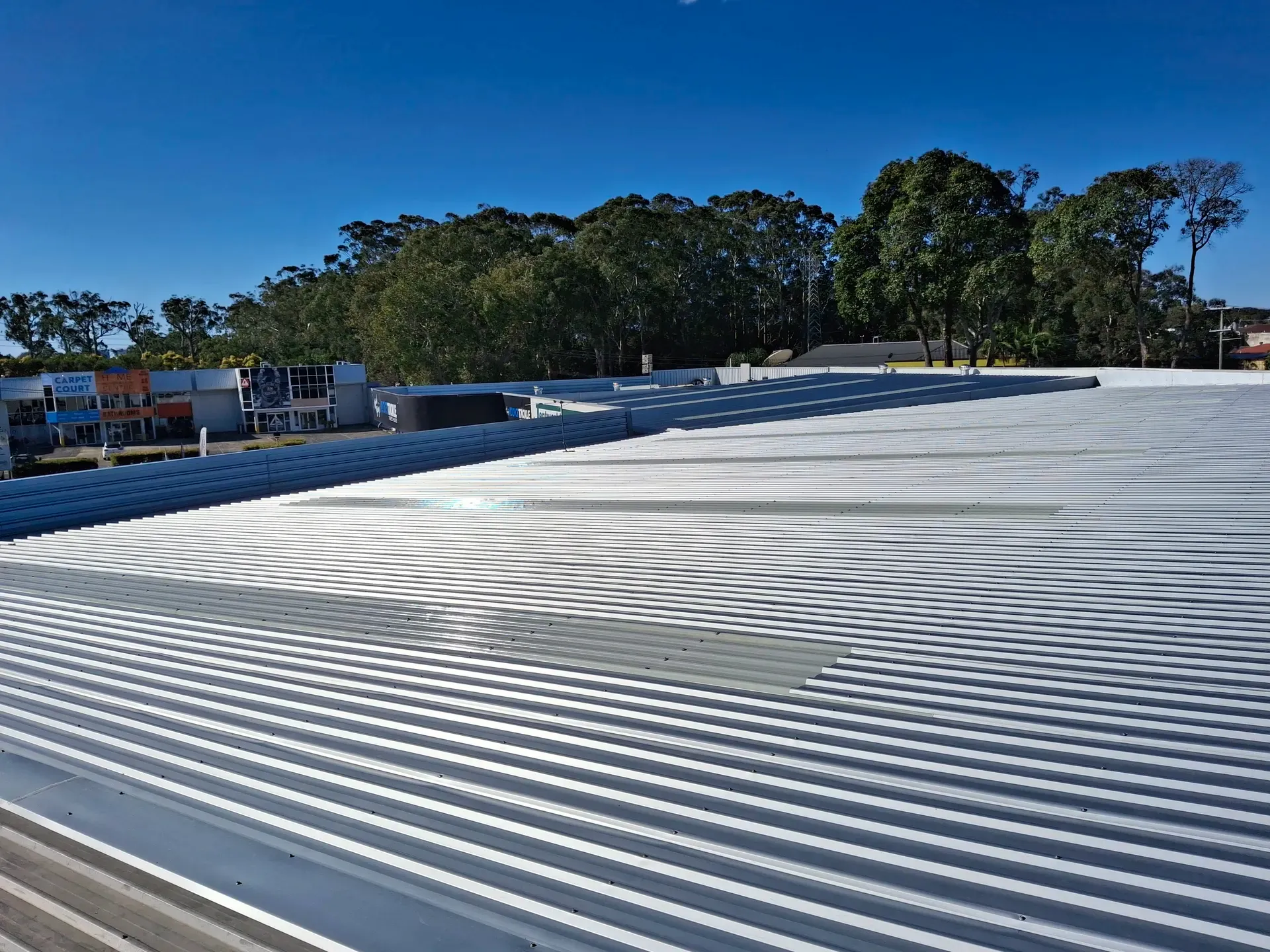 A corrugated metal roof in daylight, trees in background, clear blue sky.
