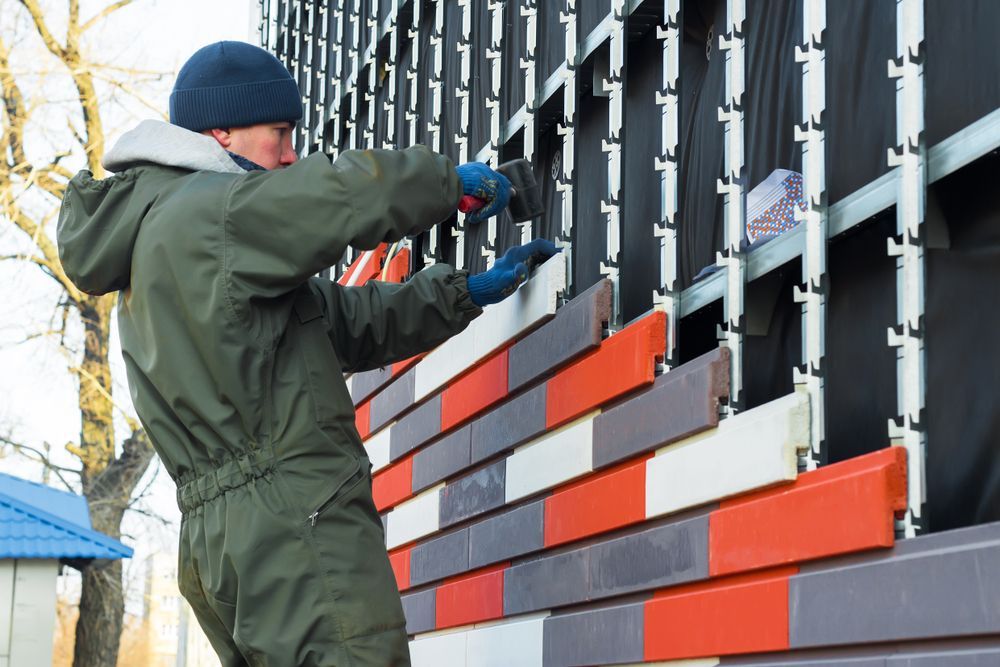 Man installing colorful brick-like siding on a building exterior.