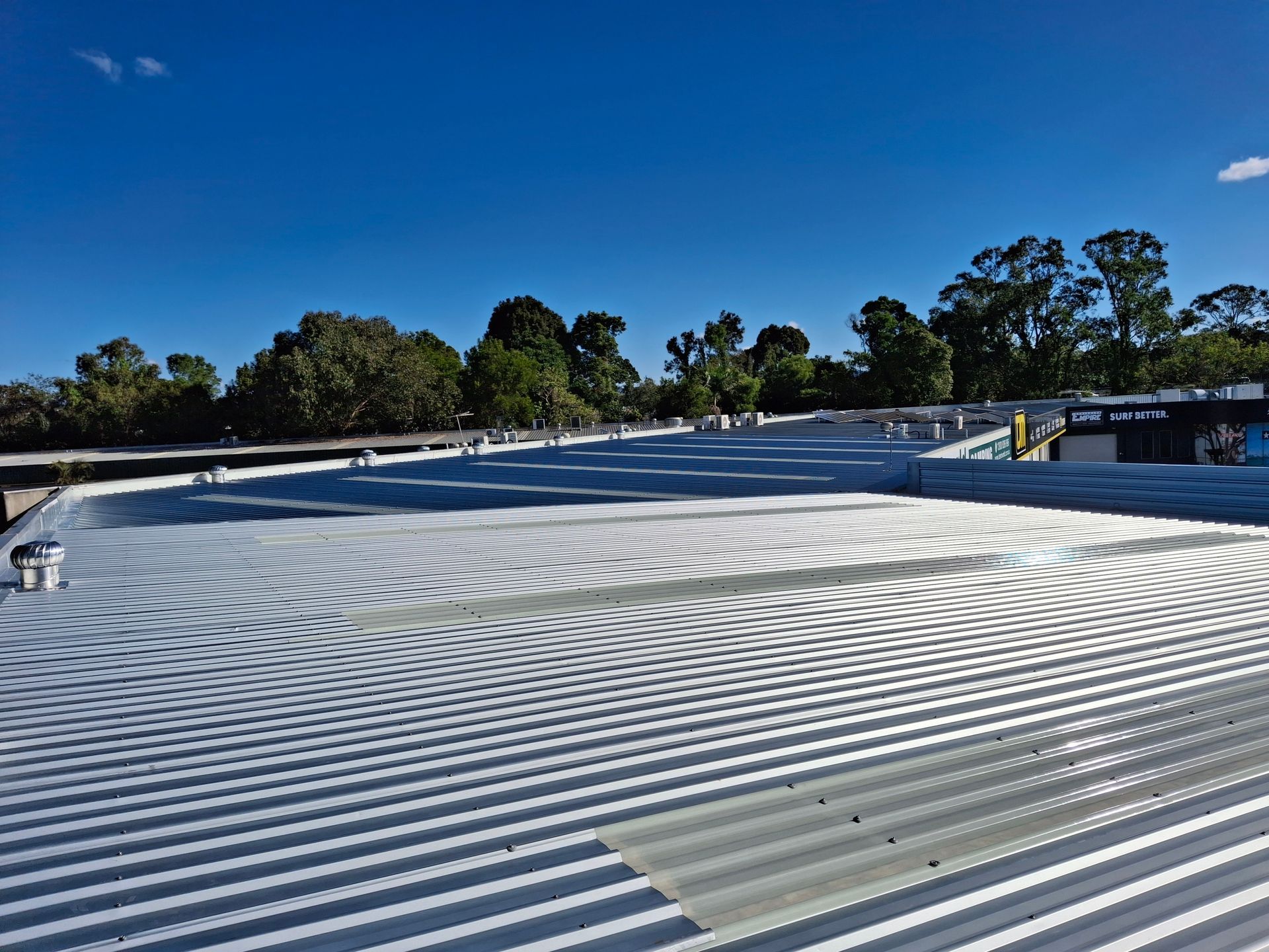 Corrugated metal roof, painted white, with trees and a blue sky in the background.