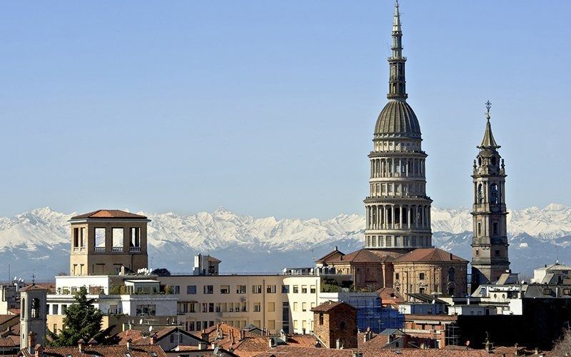 Skyline della città con l'alta torre della cattedrale e le montagne innevate sullo sfondo.