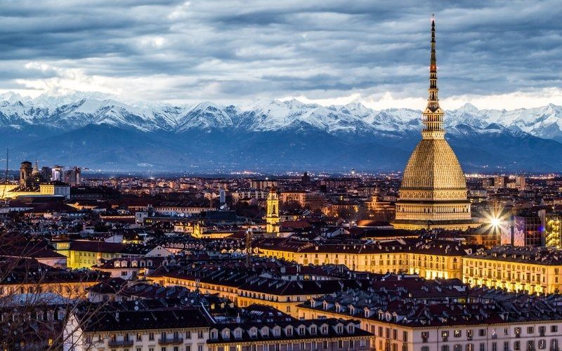 Paesaggio urbano di Torino, Italia, con la Mole Antonelliana ben illuminata e le montagne innevate sullo sfondo.