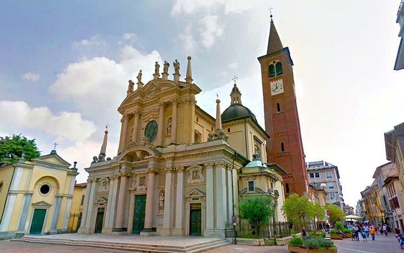 Chiesa barocca con alto campanile in mattoni e piazza aperta a Saronno, Italia.