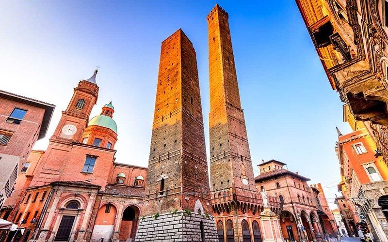 A Bologna, in Italia, si ergono due torri medievali con una chiesa sullo sfondo.