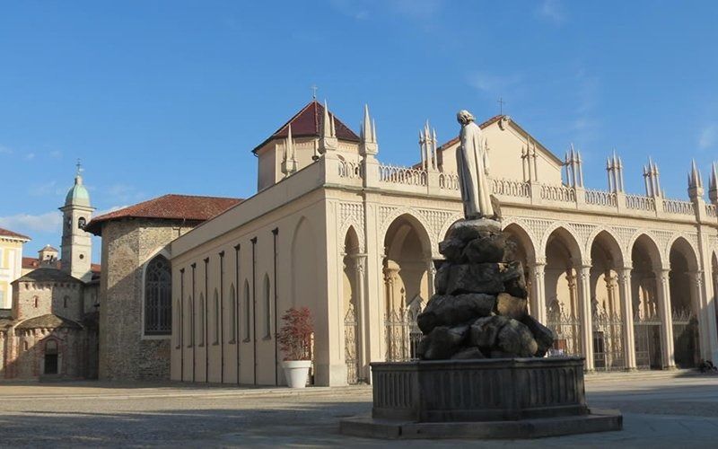 Edificio in pietra con archi e statua in una giornata di sole.