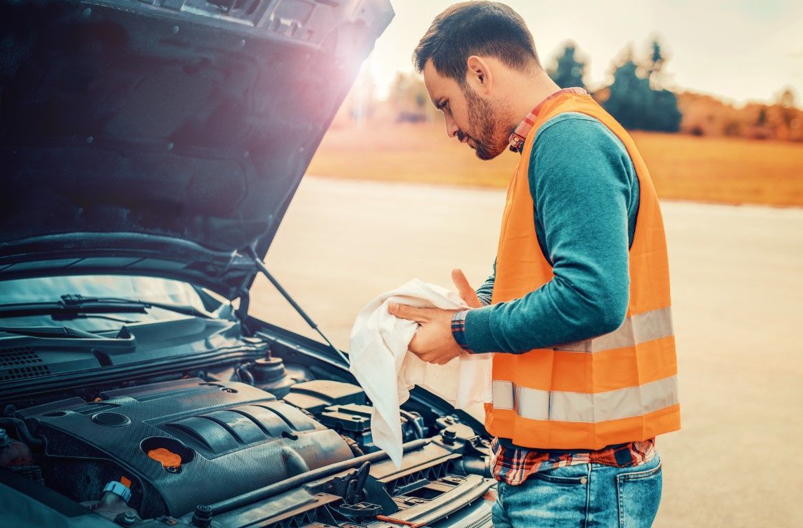 Man in orange safety vest checking car engine with hood open on roadside