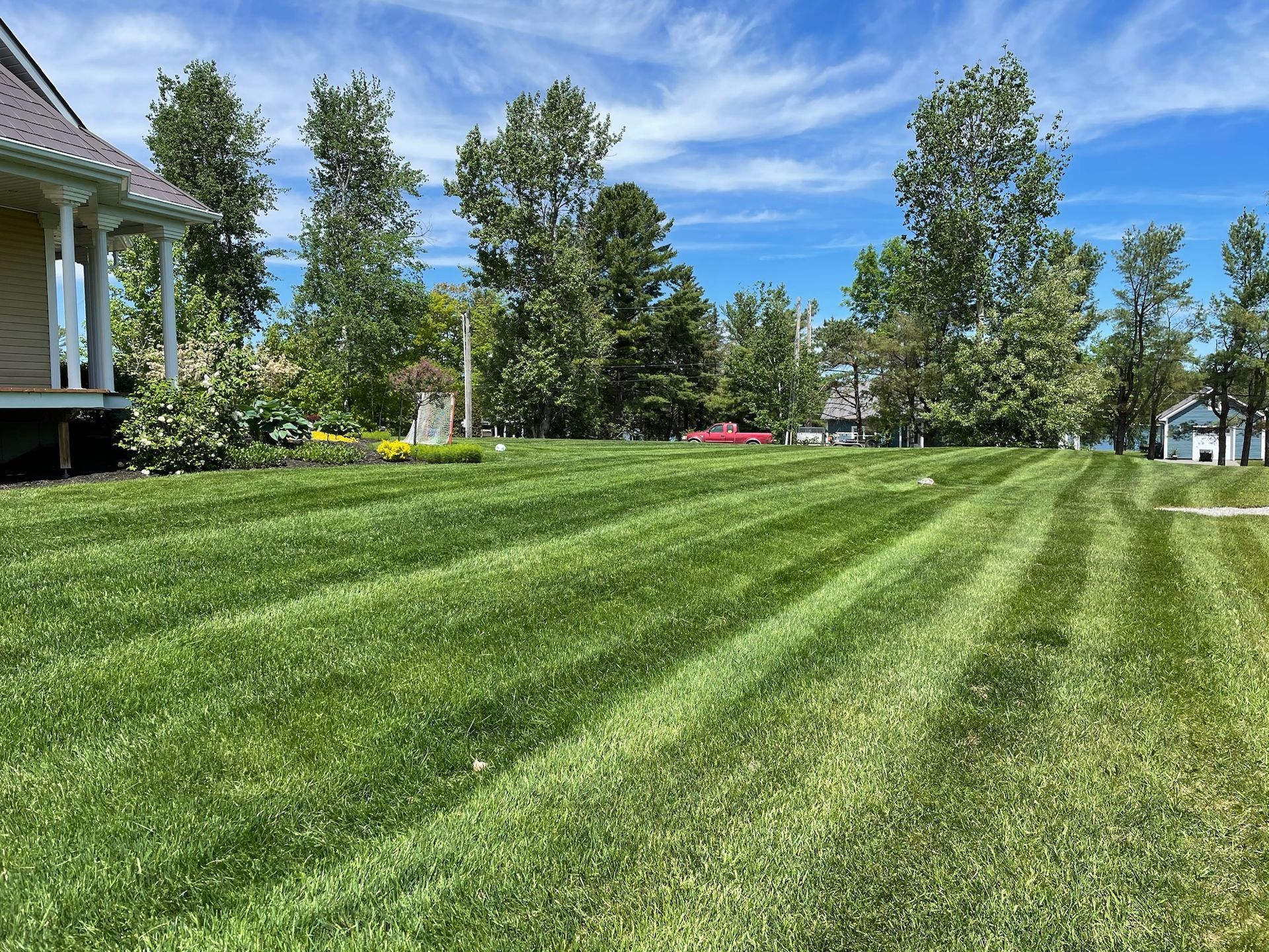 Pelouse tondue en diagonale à côté d'un porche, d'arbres et d'un ciel d'un bleu éclatant